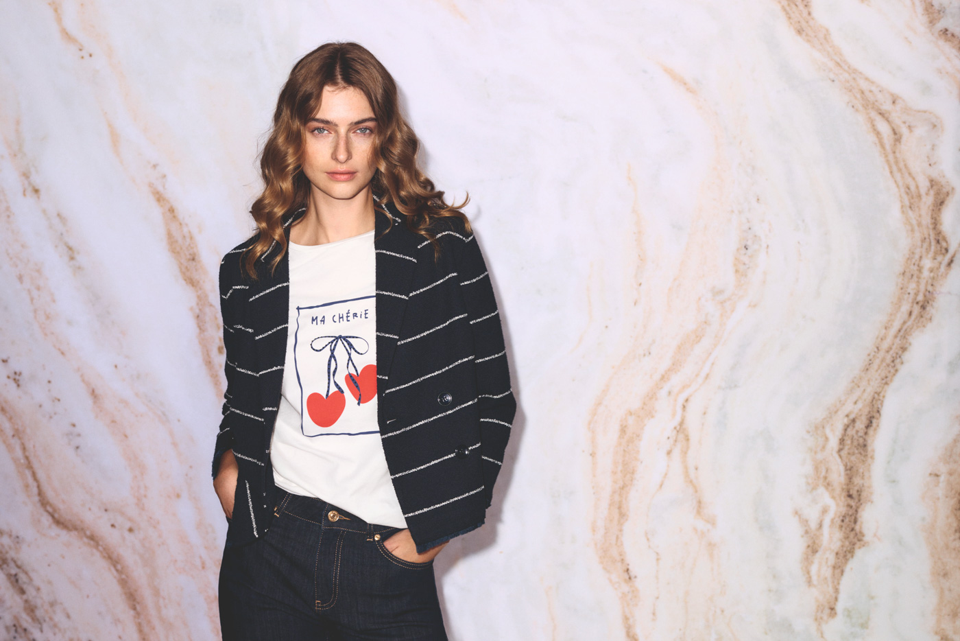 Frau mit einem weißen Shirt und einer gestreiften Jacke vor einer Wand